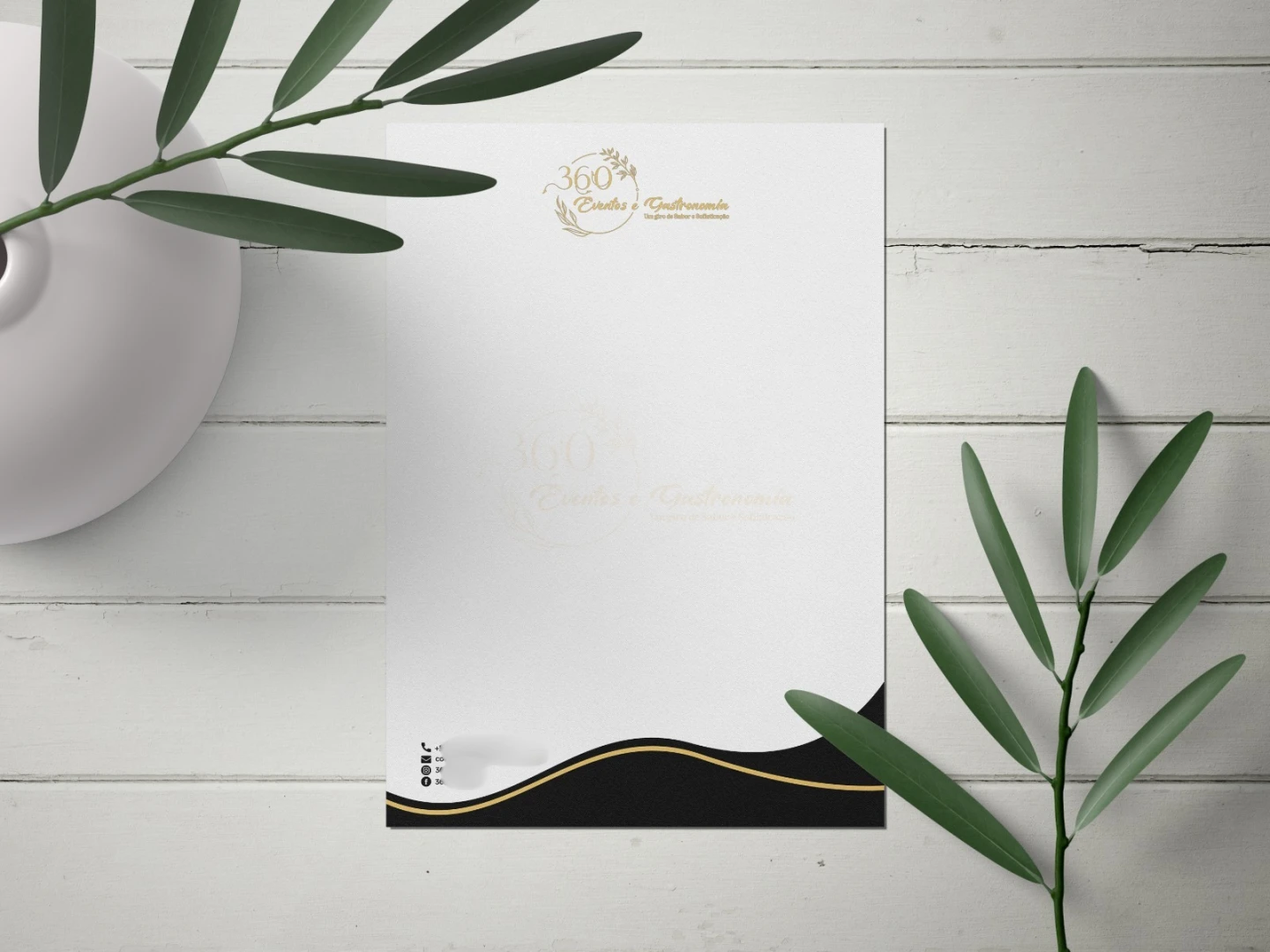 Papel timbrado corporativo para empresa de gastronomia com acabamento preto e dourado sobre mesa de madeira branca com folhas verdes.