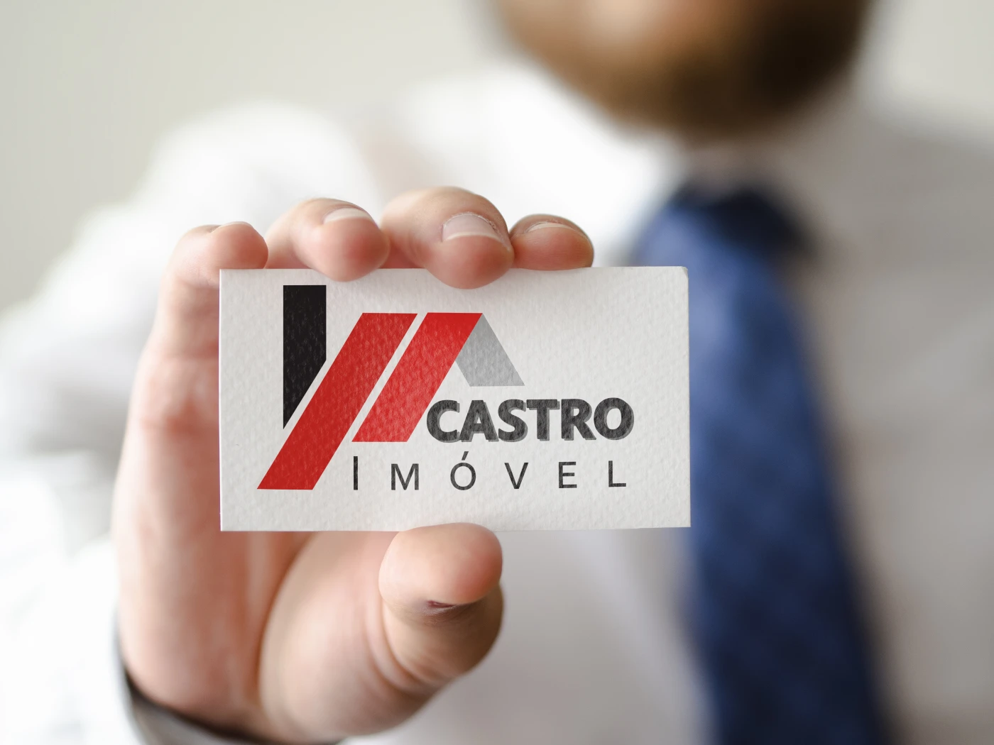 Cartão de visitas sendo segurado exibindo o logo da Castro Imóvel em cores preto e vermelho.
